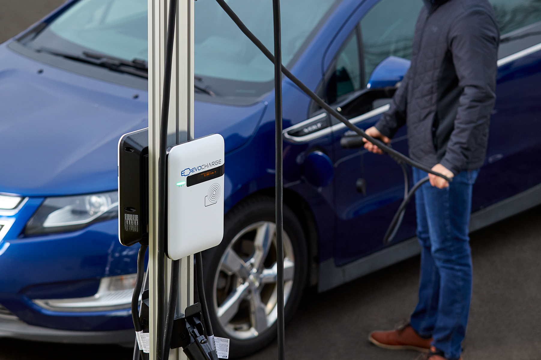 An EvoCharge charger in the forefront with a man charging his car in the background