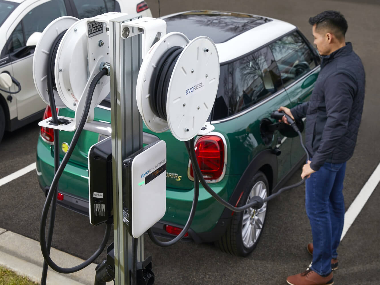 A man charging his green mini cooper with an EvoReel and EvoCharge charger