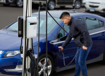 An EvoCharge charger in the forefront with a man charging his car in the background