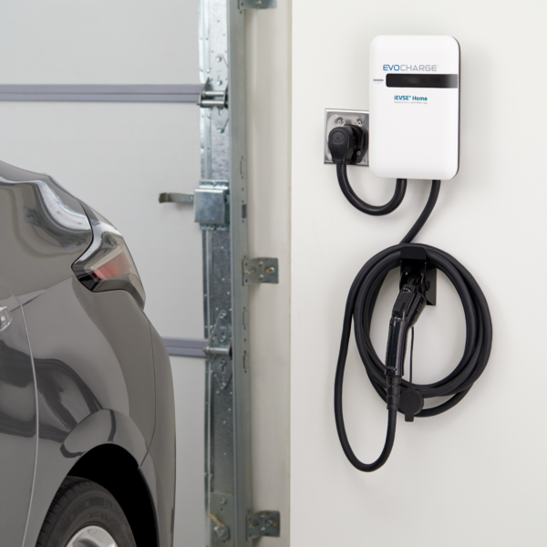 EvoCharge iEVSE Home charger hanging on a wall in a garage next to a grey car.